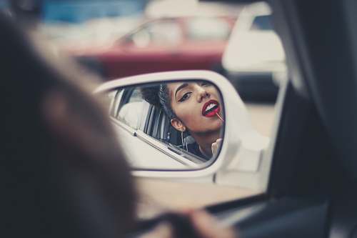 car mirror woman putting liquid lipstick on her lips while looking at vehicle's mirror during daytime female